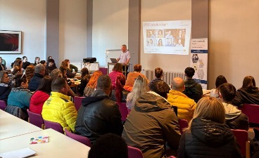 Gäste im Willkommens-Café Fürth Mehrere Gäste sind von hinten zu sehen und schauen nach vorne zum Redner, der vor einer Präsentation steht.