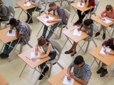 Mehrere junge Menschen sitzen an Einzeltischen und schreiben auf ein Blatt Papier.