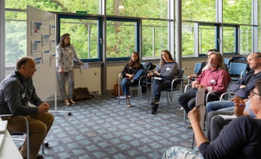 KAUSA Workshop in Günzburg Die beiden Moderator*innen sind von Gästen umringt, die in einem Halbkreis sitzen.