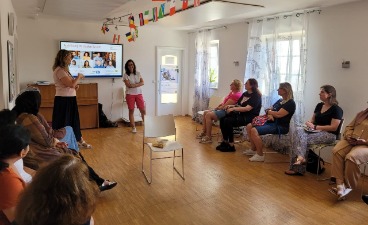 Frauen im Mehrgenerationenhaus Eine Gruppe von Frauen sitzt an kreisförmig angeordneten Stühlen. Sie blicken nach vorne zur Rednerin vor einer Präsentation.